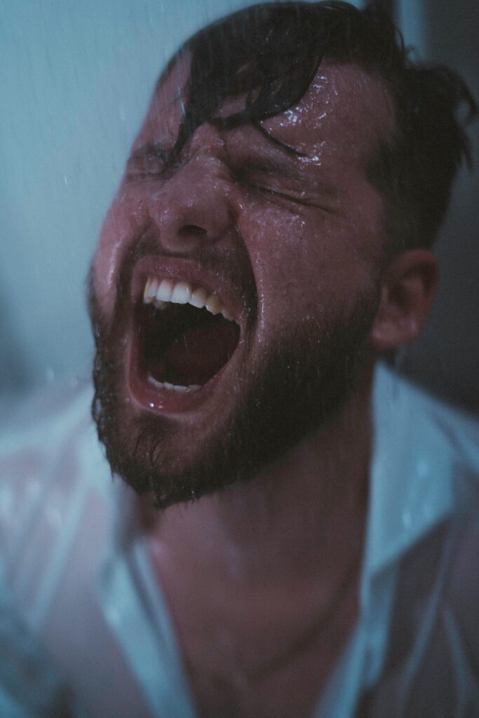 A dramatic shot of a man under a shower, showcasing intense emotions and water streaming down.