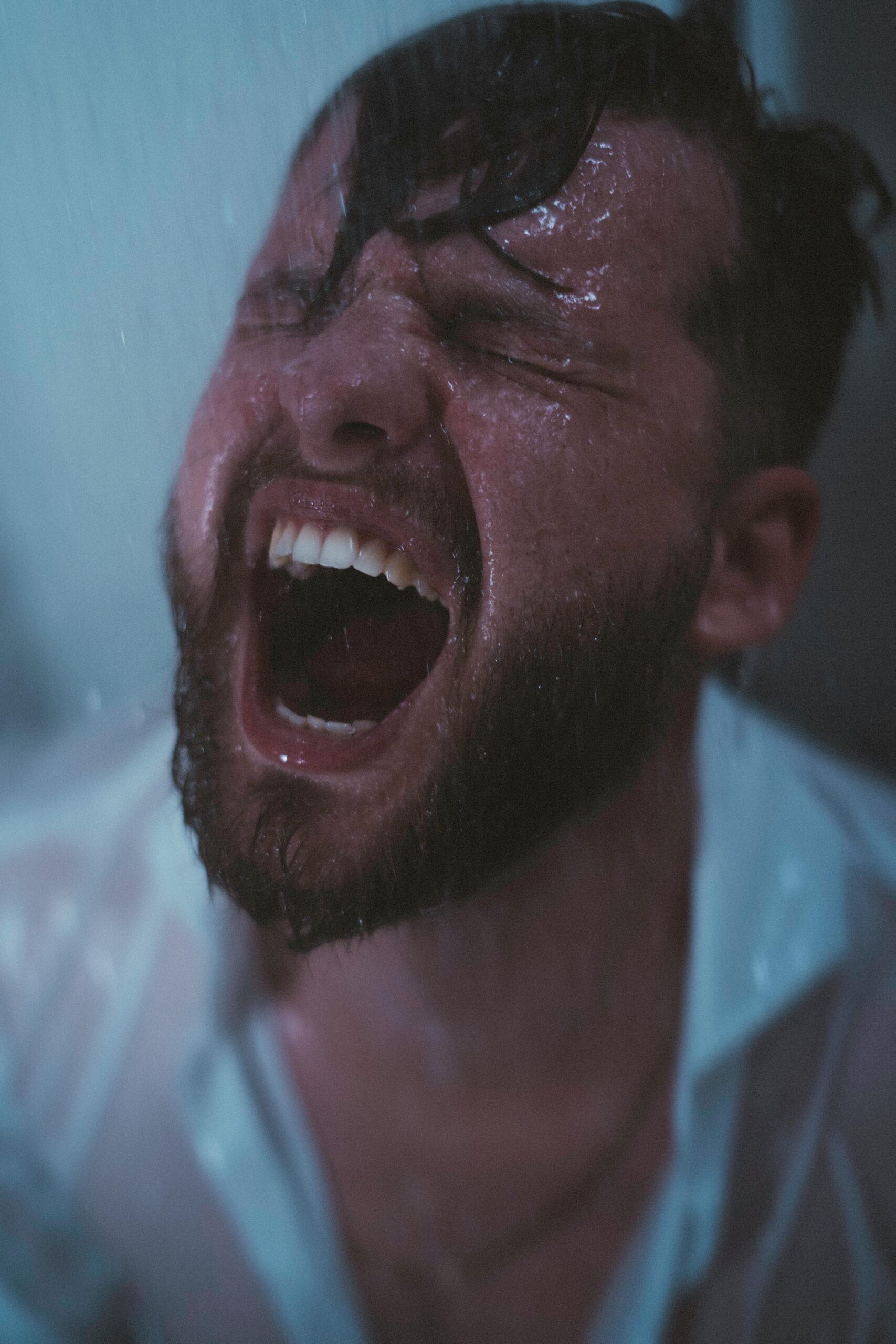 A dramatic shot of a man under a shower, showcasing intense emotions and water streaming down.